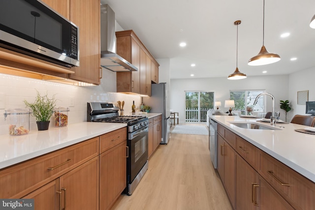 kitchen featuring sink, decorative light fixtures, light wood-type flooring, stainless steel appliances, and wall chimney range hood