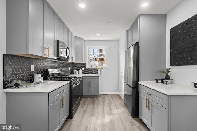 kitchen featuring refrigerator, gray cabinetry, tasteful backsplash, gas range, and light wood-type flooring