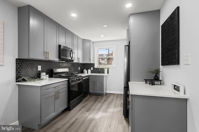 kitchen featuring sink, black gas stove, gray cabinetry, light hardwood / wood-style floors, and decorative backsplash