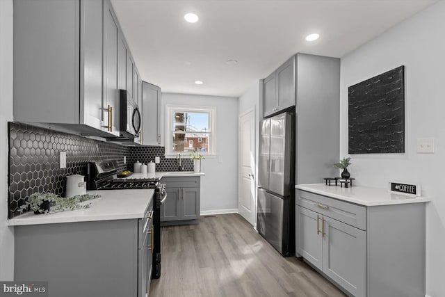 kitchen with gray cabinets, sink, decorative backsplash, stainless steel appliances, and light hardwood / wood-style flooring