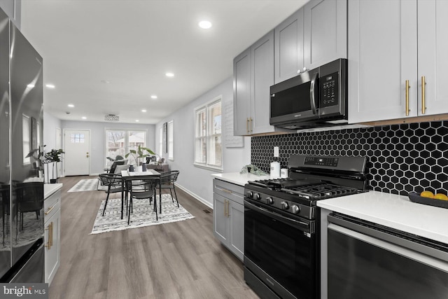 kitchen featuring tasteful backsplash, light wood-type flooring, gray cabinets, and appliances with stainless steel finishes