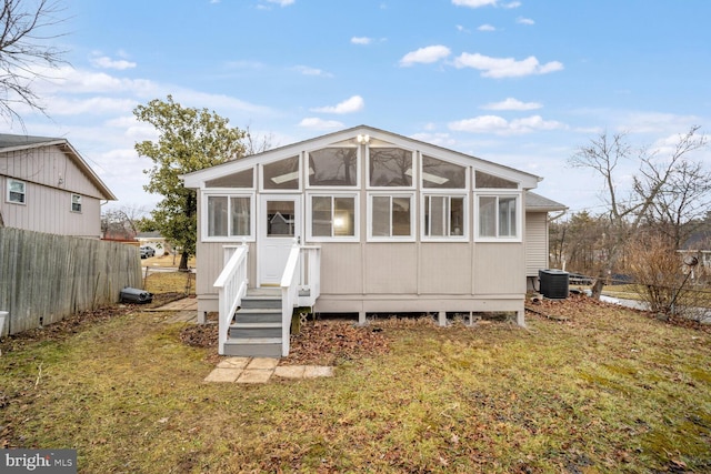 rear view of house with central AC unit and a lawn