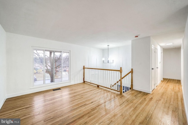 empty room with light hardwood / wood-style floors and a chandelier