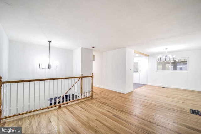 empty room with a notable chandelier and light hardwood / wood-style floors