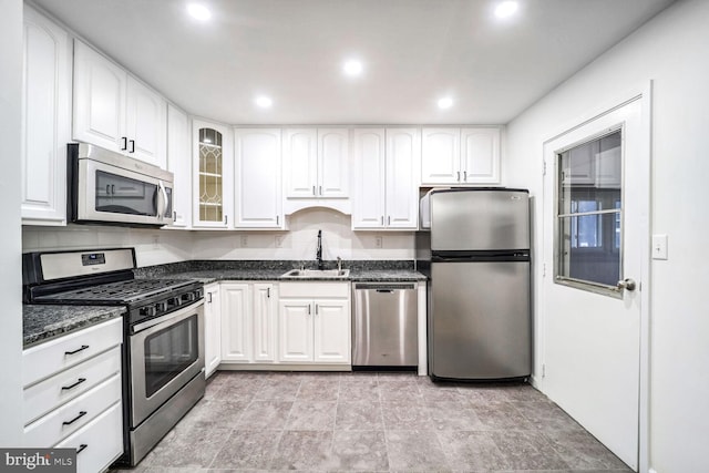 kitchen with sink, backsplash, stainless steel appliances, white cabinets, and dark stone counters