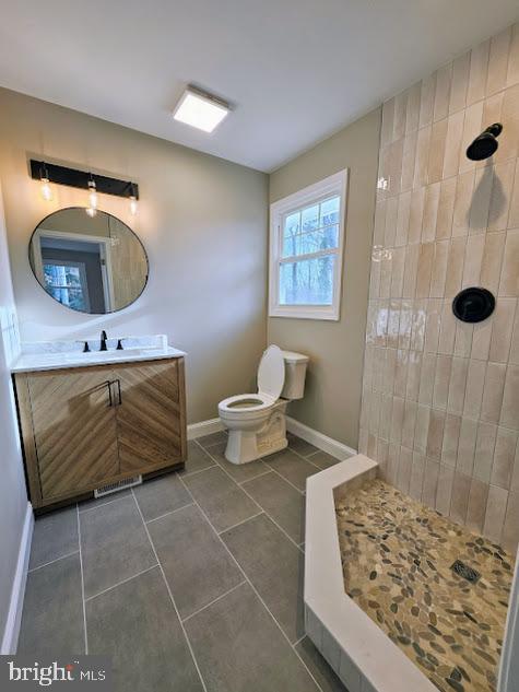 bathroom with a tile shower, vanity, tile patterned flooring, and toilet