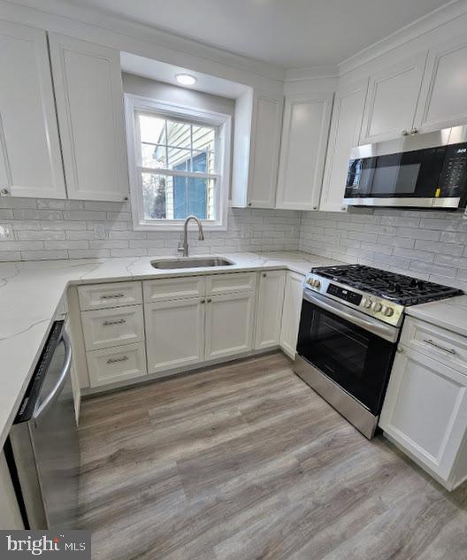 kitchen featuring sink, white cabinets, light stone counters, stainless steel appliances, and light wood-type flooring