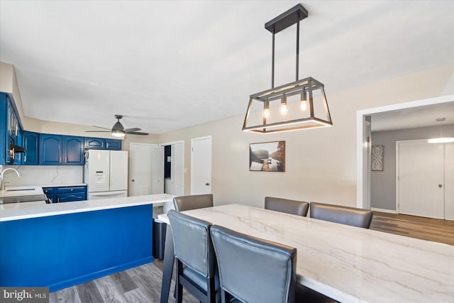 kitchen featuring pendant lighting, blue cabinets, a kitchen bar, white refrigerator with ice dispenser, and kitchen peninsula