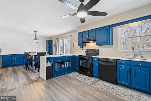 kitchen featuring pendant lighting, sink, black appliances, light hardwood / wood-style floors, and blue cabinets