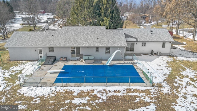 snow covered rear of property featuring a pool with hot tub and a patio area