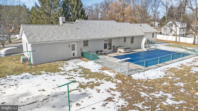 snow covered back of property with a swimming pool with hot tub and a patio