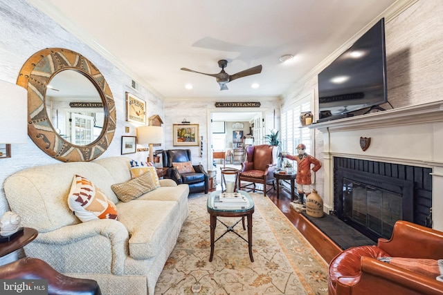 living room featuring crown molding, ceiling fan, hardwood / wood-style floors, and a brick fireplace