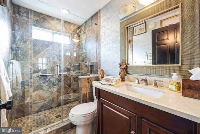 bathroom with vanity, toilet, a shower with door, and tile walls