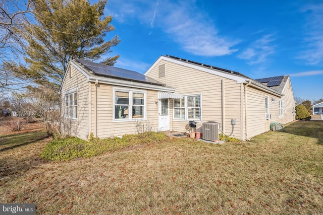 rear view of property featuring cooling unit, a lawn, and solar panels