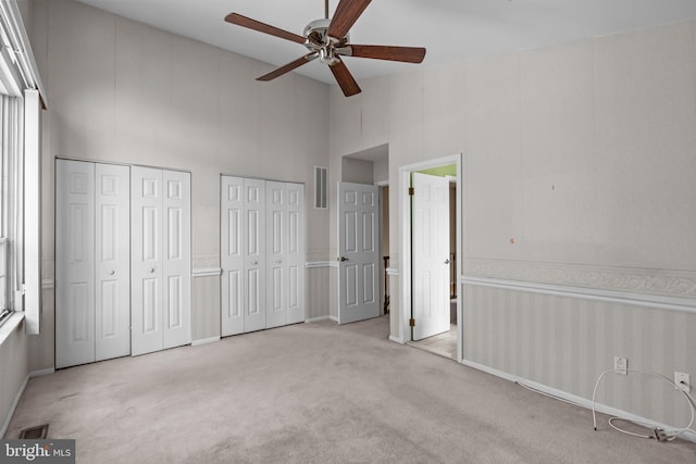 unfurnished bedroom with light carpet, two closets, high vaulted ceiling, and ceiling fan