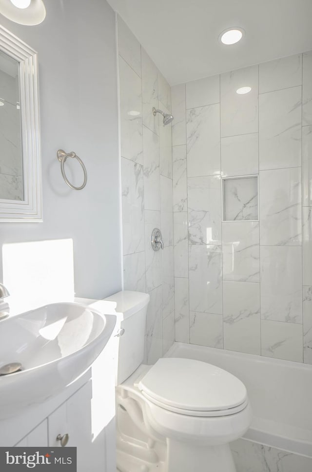 bathroom featuring vanity, a tile shower, and toilet