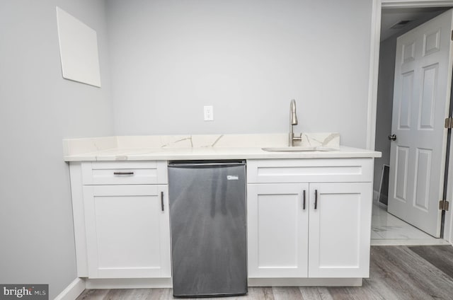 kitchen with dishwashing machine, sink, white cabinetry, and light stone countertops