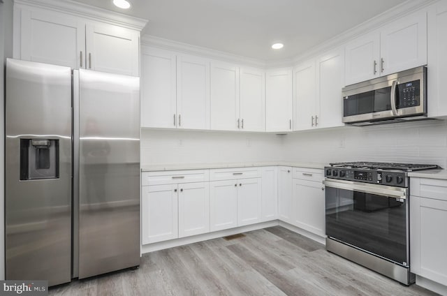 kitchen with decorative backsplash, light hardwood / wood-style flooring, white cabinets, and appliances with stainless steel finishes