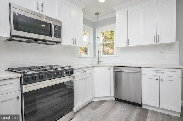 kitchen featuring sink, white cabinetry, crown molding, decorative light fixtures, and appliances with stainless steel finishes