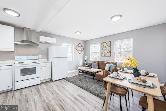 kitchen with an AC wall unit, light wood-type flooring, white appliances, wall chimney range hood, and white cabinets