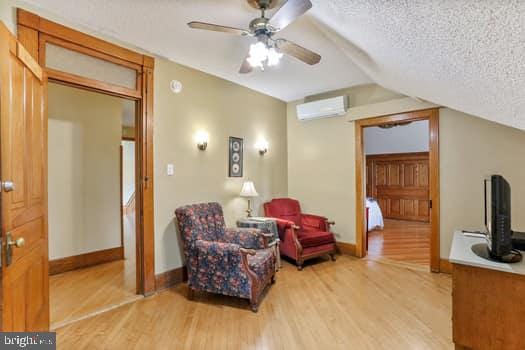 living area featuring lofted ceiling, light hardwood / wood-style floors, a textured ceiling, and an AC wall unit