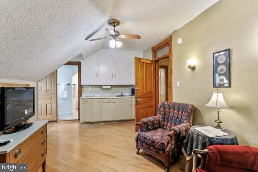 interior space featuring lofted ceiling, ceiling fan, a textured ceiling, and light wood-type flooring