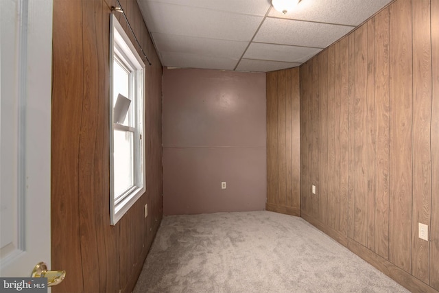 carpeted spare room with a paneled ceiling and wood walls