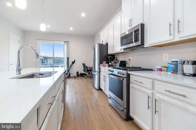 kitchen featuring pendant lighting, sink, appliances with stainless steel finishes, white cabinetry, and light stone counters