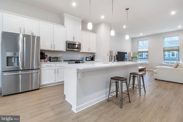 kitchen featuring hanging light fixtures, appliances with stainless steel finishes, a kitchen island with sink, and white cabinets