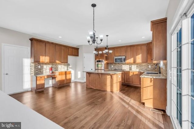 kitchen with sink, dark hardwood / wood-style flooring, a kitchen island, a notable chandelier, and stainless steel appliances