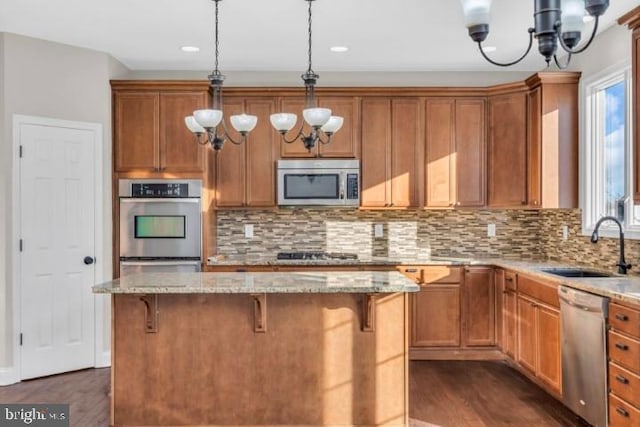 kitchen featuring stainless steel appliances, a center island, sink, and light stone counters