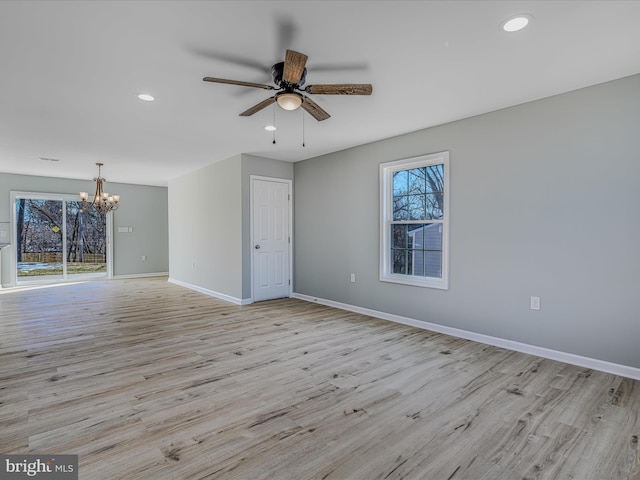 empty room with ceiling fan with notable chandelier, a wealth of natural light, and light hardwood / wood-style floors