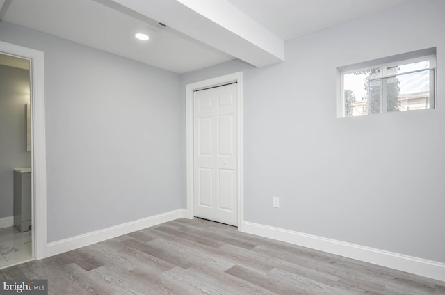 unfurnished bedroom with light hardwood / wood-style floors, a closet, beamed ceiling, and ensuite bathroom