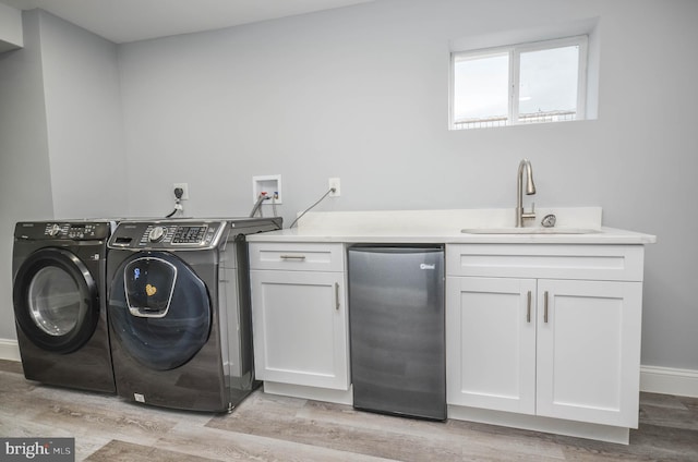 clothes washing area with sink, cabinets, light hardwood / wood-style floors, and washer and dryer