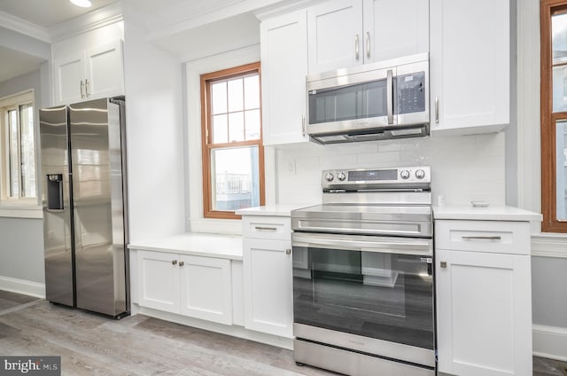 kitchen featuring light wood-type flooring, ornamental molding, appliances with stainless steel finishes, decorative backsplash, and white cabinets