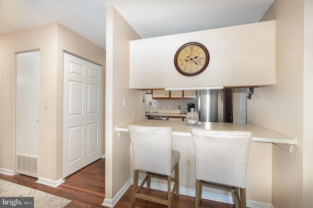 kitchen featuring a kitchen bar, stainless steel refrigerator, dark hardwood / wood-style flooring, kitchen peninsula, and backsplash