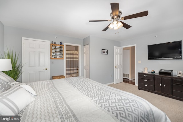 bedroom featuring ceiling fan, light colored carpet, and ensuite bath