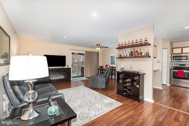 living room featuring dark wood-type flooring, ceiling fan, and indoor bar