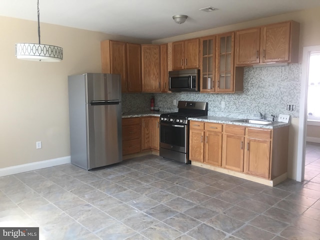 kitchen with appliances with stainless steel finishes, decorative light fixtures, sink, decorative backsplash, and light stone counters