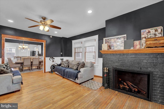 living room with a brick fireplace, ceiling fan with notable chandelier, and light hardwood / wood-style flooring