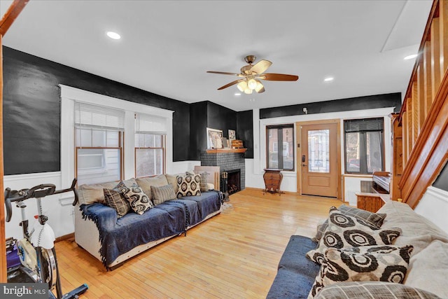 living room featuring ceiling fan, plenty of natural light, a brick fireplace, and light hardwood / wood-style flooring