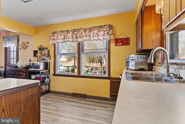 kitchen with visible vents, a sink, stainless steel microwave, light wood-style floors, and brown cabinetry