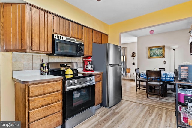 kitchen featuring tasteful backsplash, appliances with stainless steel finishes, brown cabinetry, and light wood-style floors