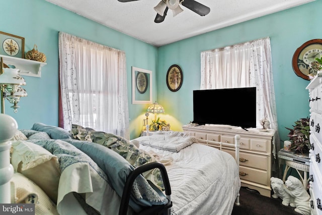 bedroom with a textured ceiling, ceiling fan, and dark colored carpet