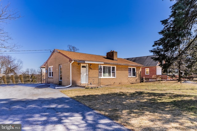 view of front of house featuring driveway, a front lawn, fence, brick siding, and a chimney