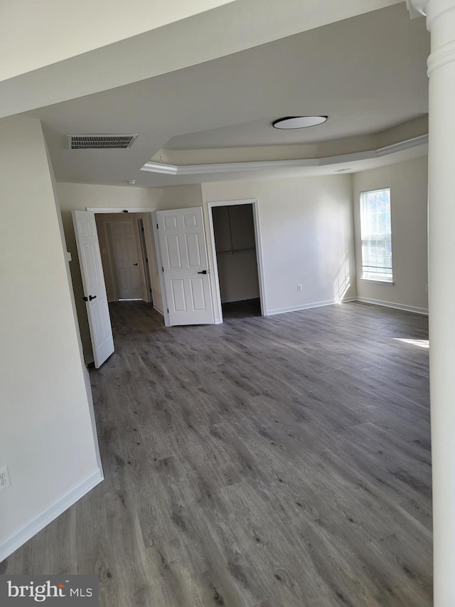 empty room featuring a tray ceiling, hardwood / wood-style flooring, and ornate columns