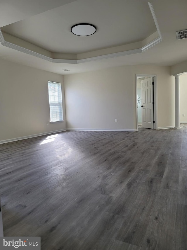 spare room with a tray ceiling, decorative columns, and dark hardwood / wood-style floors