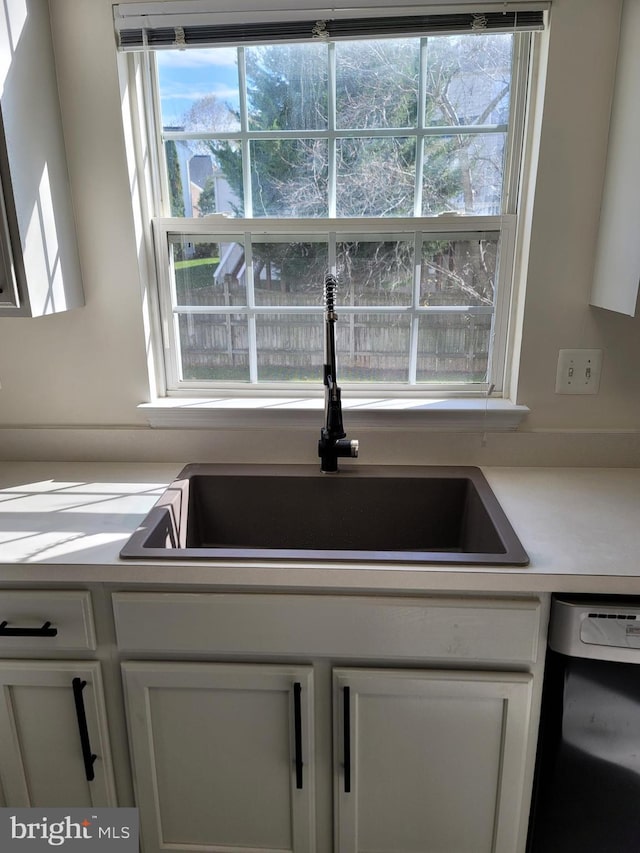 kitchen with white cabinetry, black dishwasher, and sink