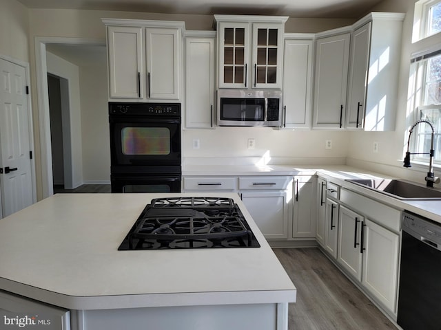 kitchen with sink, light hardwood / wood-style flooring, white cabinetry, a center island, and black appliances