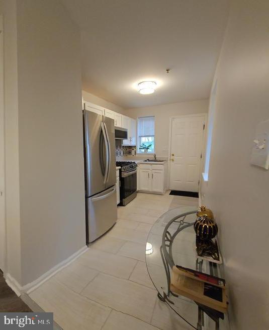 kitchen with light countertops, appliances with stainless steel finishes, white cabinets, a sink, and baseboards